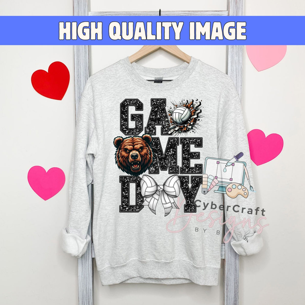 A light gray crewneck sweatshirt hanging on a wooden hanger, featuring a 'GAMEDAY' graphic with a bear, volleyball, and gaming controller. The image has a blue banner at the top reading 'HIGH QUALITY IMAGE' and pink heart graphics on a white background.