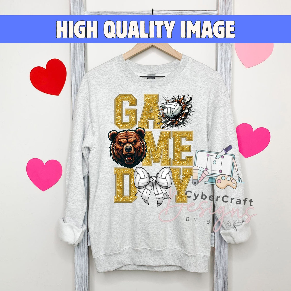 A light gray crewneck sweatshirt hanging on a wooden hanger, featuring a 'GAME DAY' graphic with a brown bear, a volleyball, a bow tie, and a paintbrush. The sweatshirt is displayed against a white wall with decorative pink and red hearts, and a blue banner at the top reads 'HIGH QUALITY IMAGE'.