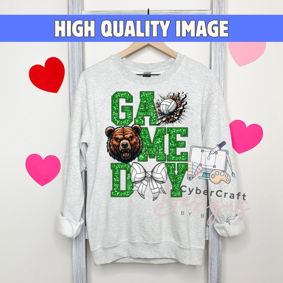 A light gray crewneck sweatshirt hanging on a wooden hanger, featuring a 'Game Day' graphic with a brown bear, green glitter-style lettering, a volleyball, and a bow tie. The background is white with pink and red heart graphics and a blue banner at the top reading 'HIGH QUALITY IMAGE'.
