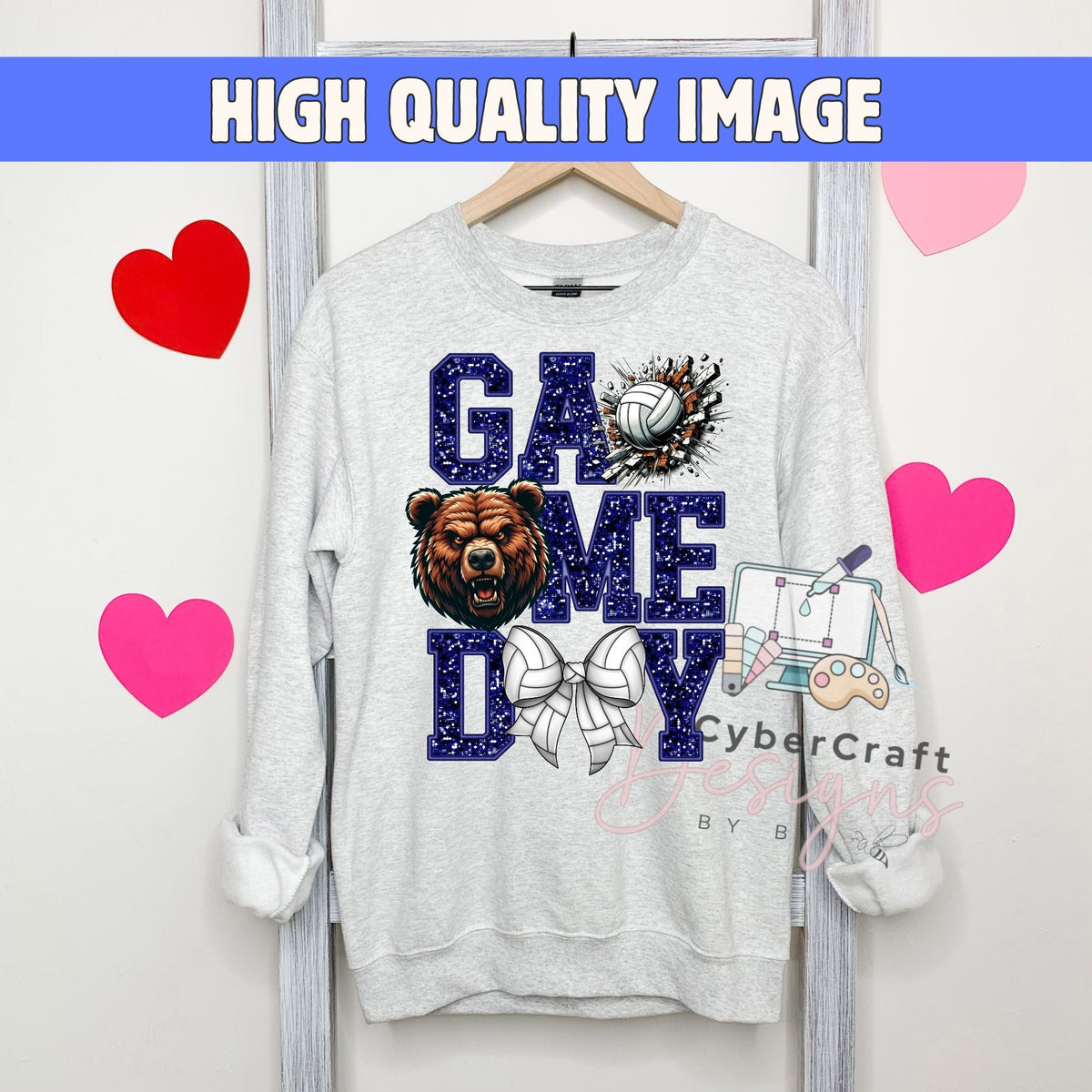 A light gray crewneck sweatshirt hanging on a wooden hanger, featuring a 'GAME DAY' graphic with a bear, volleyball, bow tie, and gaming controller. The image has a blue banner at the top reading 'HIGH QUALITY IMAGE' and pink heart graphics on the sides.