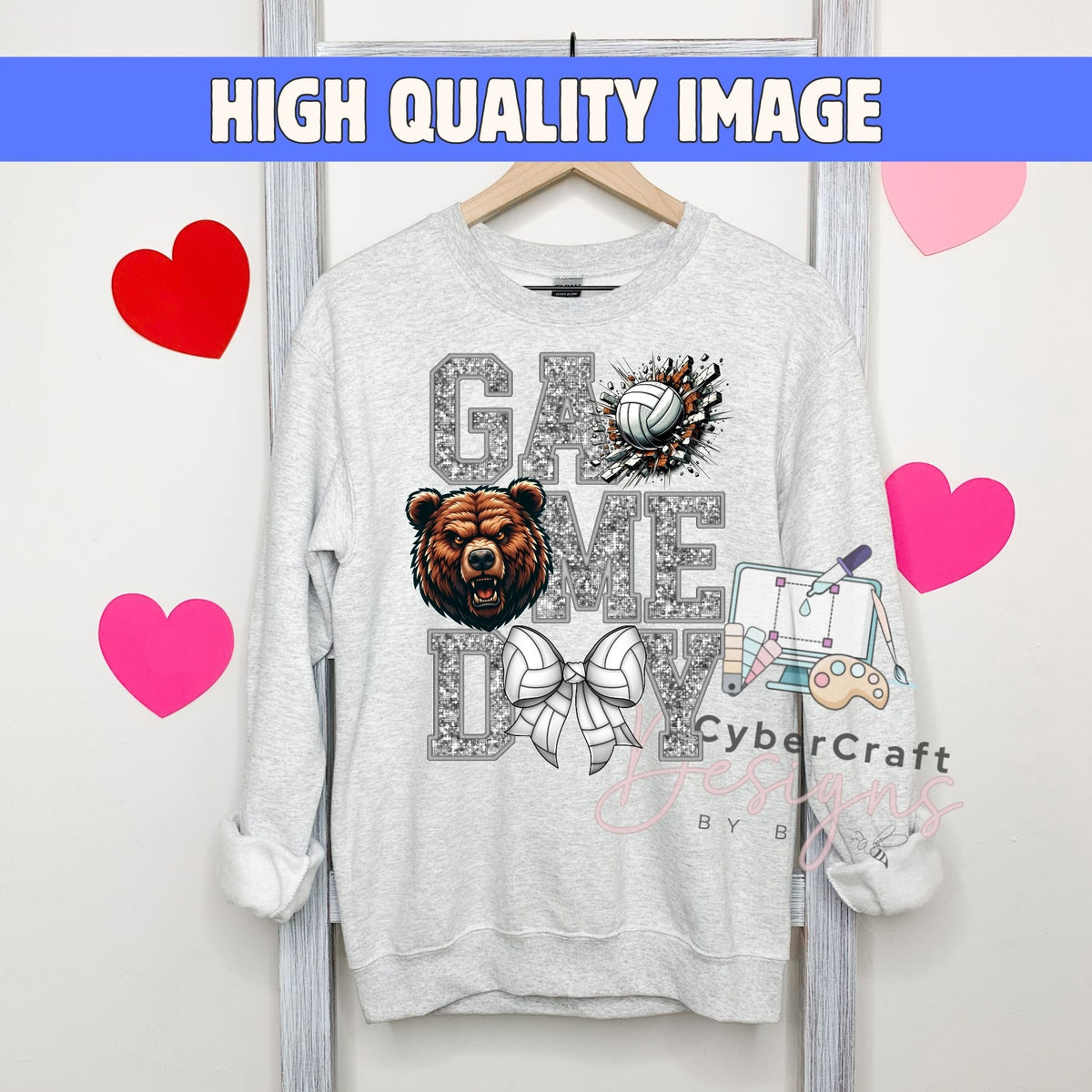 A light gray crewneck sweatshirt hanging on a wooden hanger against a white wall, featuring a 'Game Me Volley' graphic with a bear, volleyball, and bow tie. The image has a blue banner at the top reading 'HIGH QUALITY IMAGE' and pink heart graphics on the sides.