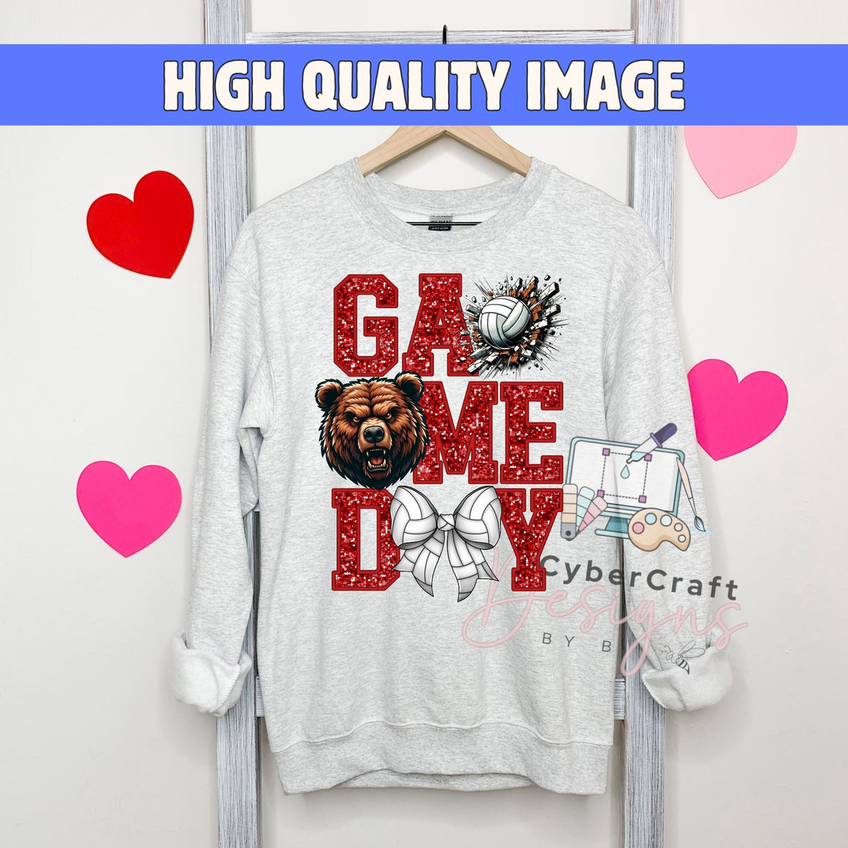 A light gray crewneck sweatshirt hanging on a wooden hanger, featuring a 'GAME DAY' graphic with a brown bear, volleyball, and sports illustrations. The image has a blue banner at the top reading 'HIGH QUALITY IMAGE' and pink heart graphics on the sides.