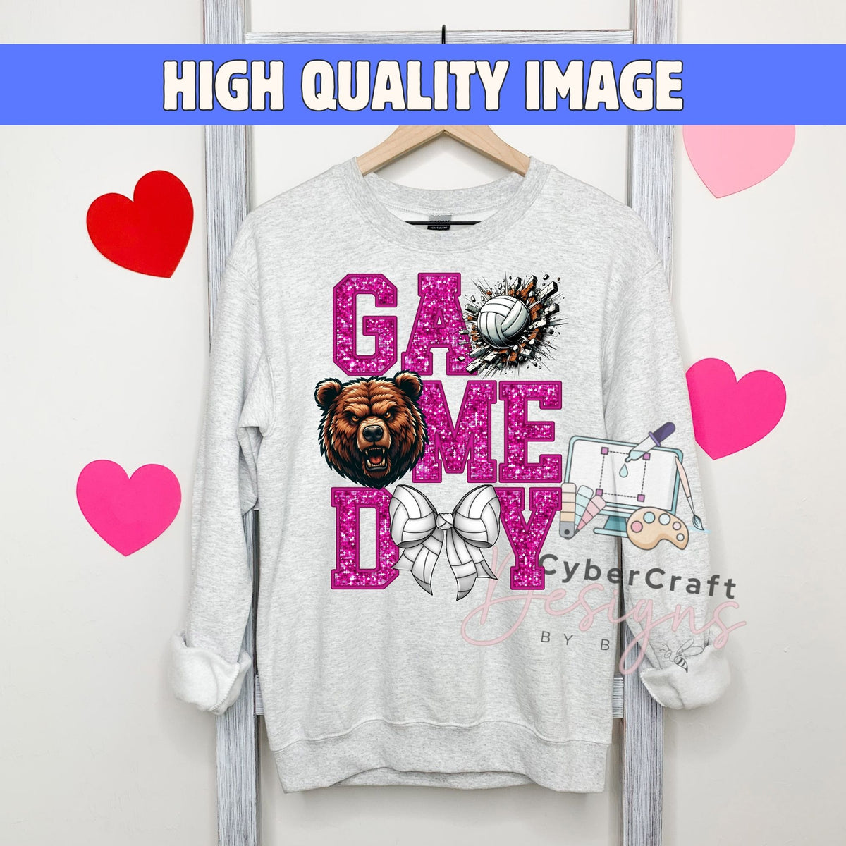 A light gray crewneck sweatshirt hanging on a wooden hanger, featuring a 'GAME ME DAY' graphic in pink glitter lettering with a bear, volleyball, and computer illustration. The image has a blue banner at the top reading 'HIGH QUALITY IMAGE' and pink heart graphics on a white background.