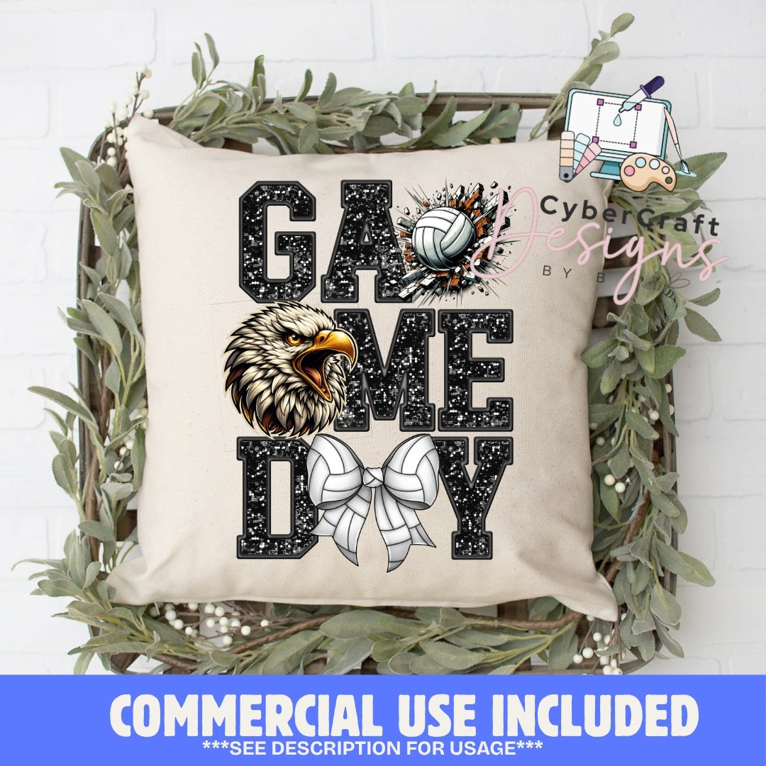 A square beige throw pillow with a 'GAME DAY' volleyball graphic, displayed in a decorative wooden crate with green foliage. The pillow features a black and white eagle head illustration and a volleyball motif.